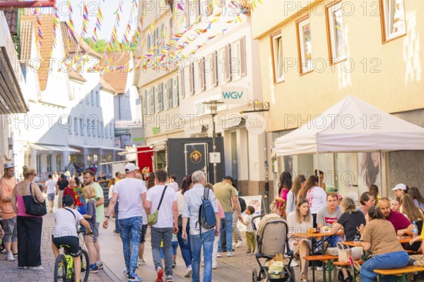 People enjoying a street festival under colourful pennants in an old town, Calw station festival,