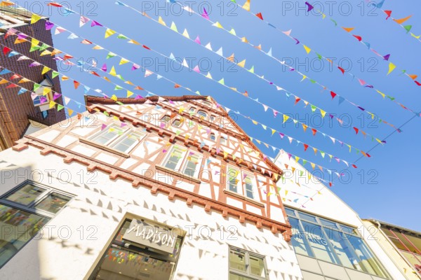 Medieval half-timbered house with colourful pennants in front of a blue sky, Calw station festival,