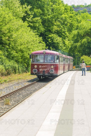 Red train travelling along a green, sunny platform in a rural setting, Calw station festival, Black