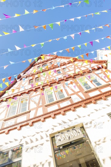Sunlit half-timbered façade with pennants against a blue sky, Calw railway station festival, Black