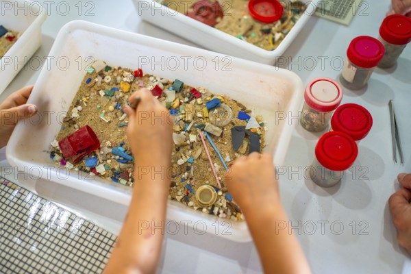 Students using tweezers collecting colorful microplastics from sand in a white plastic container