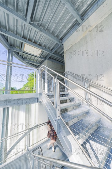 A woman on a modern metal staircase in a light-flooded interior, Zob extension with bridge