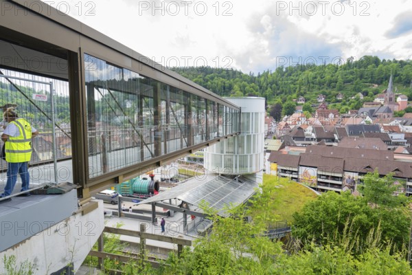 People standing on a modern bridge with a view of a hilly urban landscape, Zob extension with