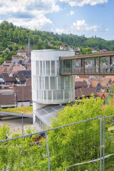 A modern building with a bridge in a town surrounded by green landscape and houses, Zob extension