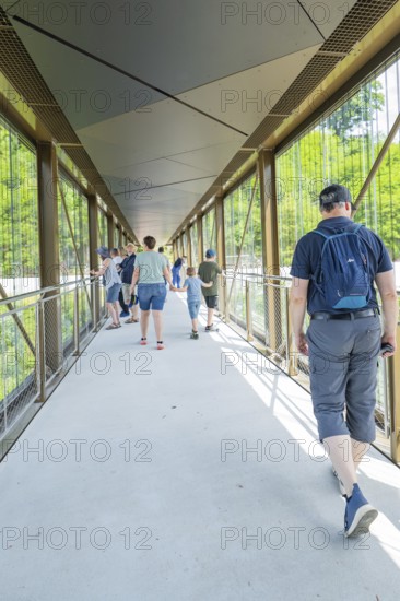 People walk over a modern glass bridge in daylight, Zob extension with bridge construction for the
