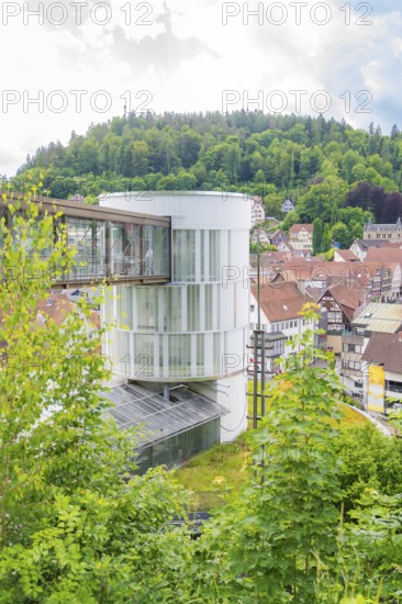 A round modern tower rises above a green, hilly urban landscape, Zob extension with bridge