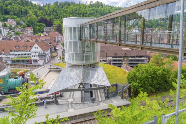 A railway station with a modern glass pedestrian overpass in a small green town, Zob extension with