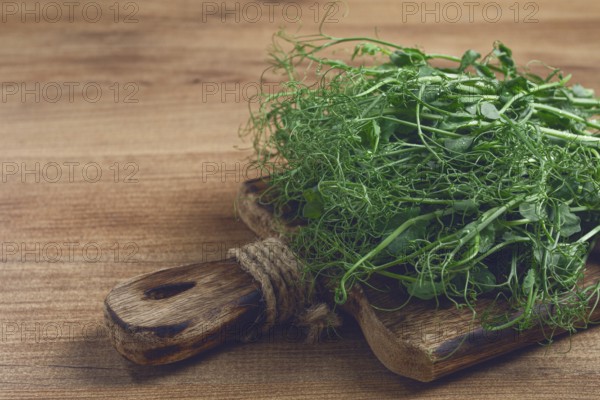 Green pea shoots with delicate tendrils are artfully placed on a textured wooden cutting board,
