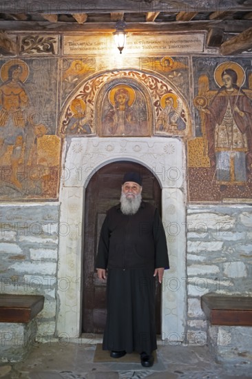Greek Orthodox priest standing by murals from 1802, Agia Marina church, Kissos, Pelion peninsula,