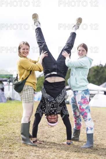A festival visitor with a handstand thanks to the support of two woman on a camping site at the