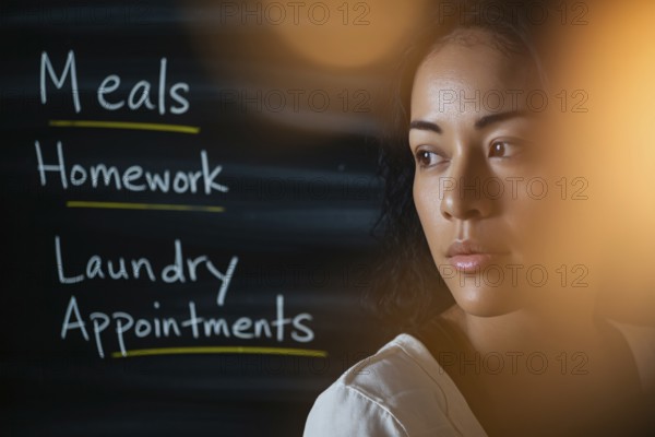 Thoughtful woman in warm light with task-filled blackboard. Concept of mental load, emotional