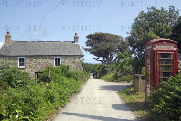 A rural scene with a stone house and red brtish telephone box along a narrow path under a blue sky,