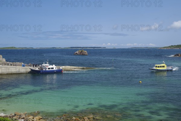 Two boats in the harbour area with a view of the open sea and distant islands under a blue sky, St