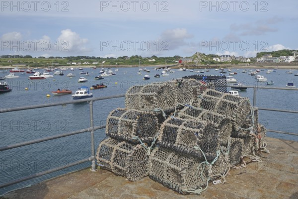 A harbour with stacked lobster pots, many boats on the water and a coastline in the background,