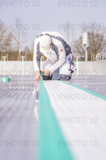 A worker kneels on the ground and precisely sticks on a green tape, renewal of the swimming lines,