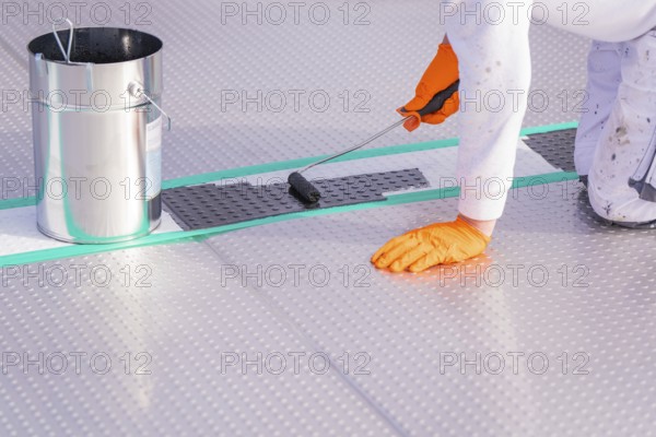A person applies paint to the floor with a paint roller, next to it a bucket, renewal of the