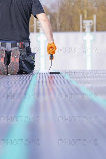 A worker kneels on the ground and applies strip paint with a paint roller, renovation of the