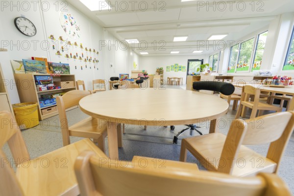 Kindergarten room with round table, wooden furniture and toys, bright atmosphere, transitional