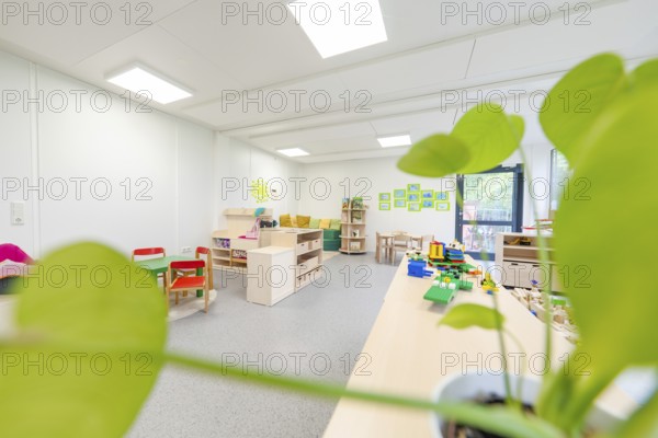 Bright classroom with play tables and a large plant in the foreground, transitional containerised