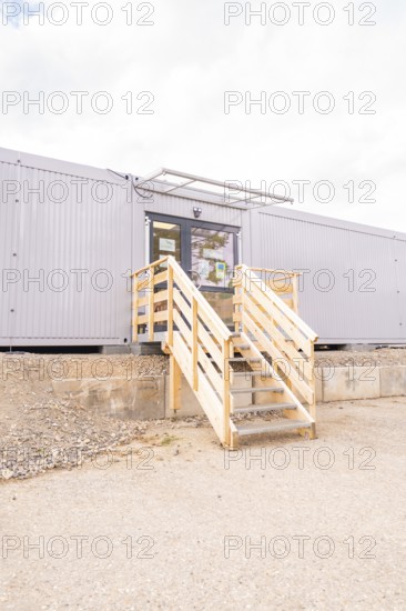 Modern entrance to a grey modular building with wooden stairs, transitional daycare centre in