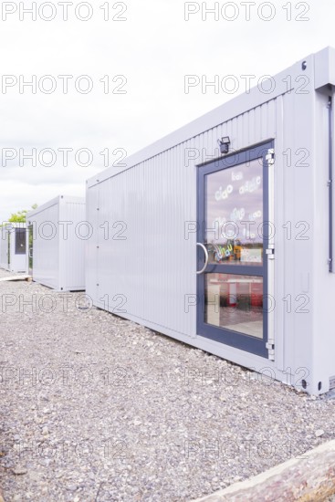Grey containers with doors in a functional outdoor area, transitional daycare centre in container