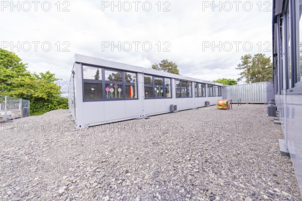 Elongated modern building with large windows and gravel floor, transitional daycare centre in