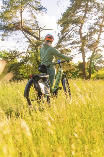 A person stands with a bicycle in the grass, surrounded by sunlight, e-bike excursion, Gechingen,