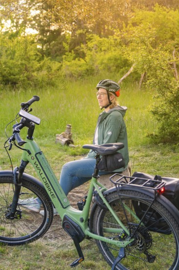 Person with helmet sitting in the sunset next to a bicycle in a meadow, surrounded by nature,