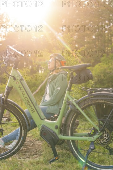 Person with helmet sitting next to a bicycle, enjoying nature in the warm sunlight, e-bike