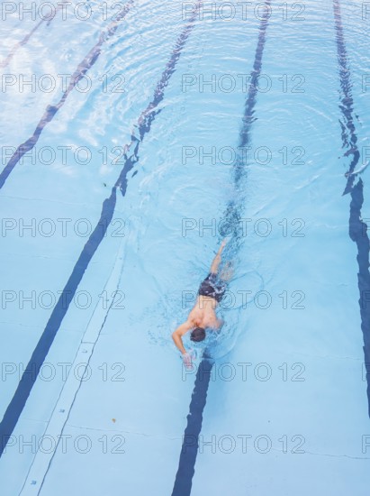 A man swims in the clear blue water of a pool along the lanes, Calw outdoor pool, Black Forest,