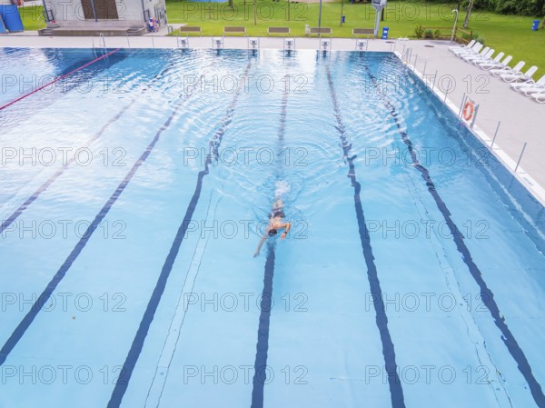 A swimmer moves alone through the lanes of a large swimming pool, Calw outdoor pool, Black Forest,