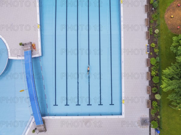 A swimmer in the large, empty pool, surrounded by paved paths and greenery, Calw outdoor pool,
