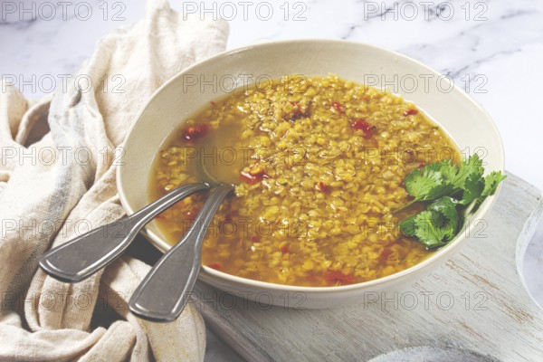 A hearty lentil soup is beautifully presented in a beige bowl, garnished with fresh herbs, placed