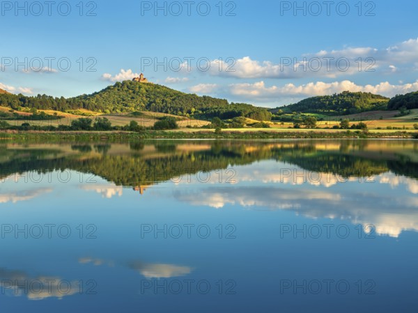 Wachsenburg Castle is reflected in the still water of a lake under a blue sky with cumulus clouds,
