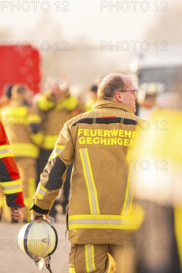 Firefighter with helmet in hand, blurred background activity, fire brigade exercise on the Hermann