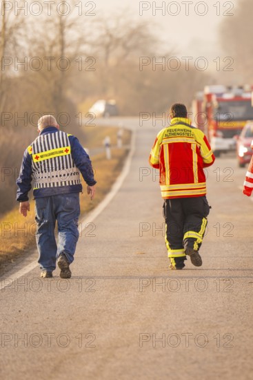 Rescue workers walk on a country road while emergency vehicles are visible in the background, fire