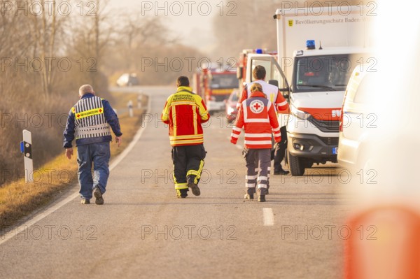 Emergency personnel from various services walk on a country road, accompanied by emergency