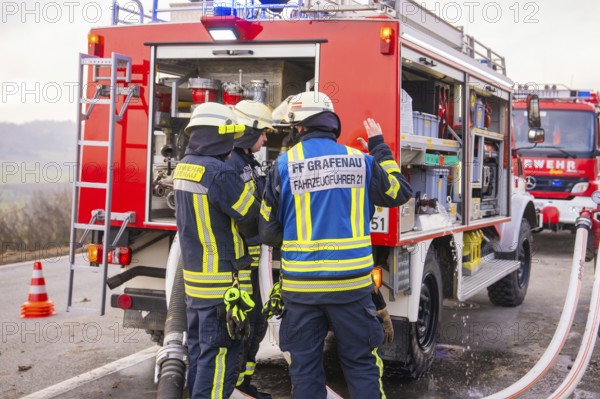 Firemen in emergency clothing stand at an emergency vehicle and check hoses, fire brigade exercise