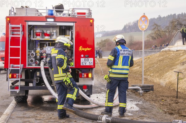 Firefighters are standing on a street near a fire truck. They are preparing hoses for use, fire
