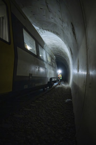 Light beam illuminates workers next to a train in a dark tunnel, fire department exercise on the