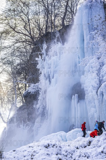 Spectators climb on the Urach waterfall full of bizarre ice formations, frozen at low winter