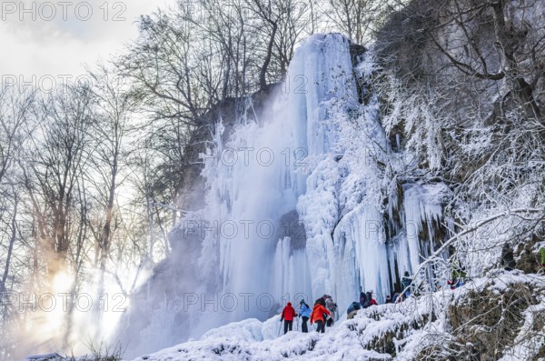 Spectators climb on the Urach waterfall full of bizarre ice formations, frozen at low winter