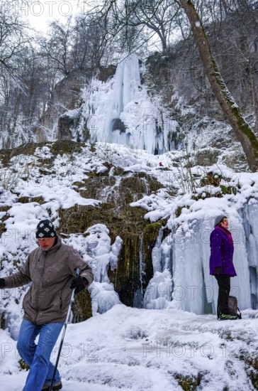 Hikers climb on the Urach waterfall full of bizarre ice formations, frozen at low winter