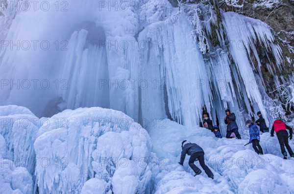 Spectators climb on the Urach waterfall full of bizarre ice formations, frozen at low winter