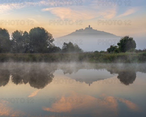 Wachsenburg Castle is reflected in the still water of a lake at sunrise, fog rises, castle of the