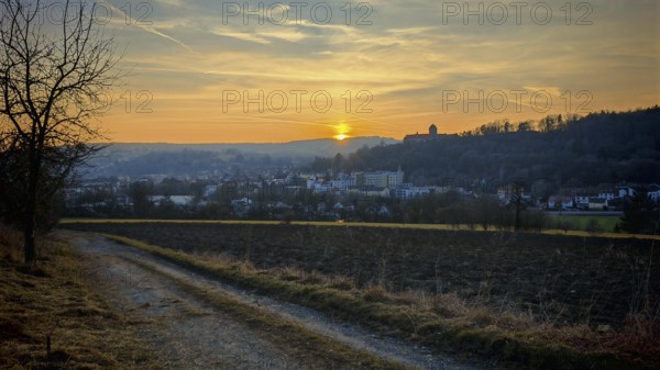 Sunset behind a small town, warm light over hills and a country road, view of Rosenberg Fortress,