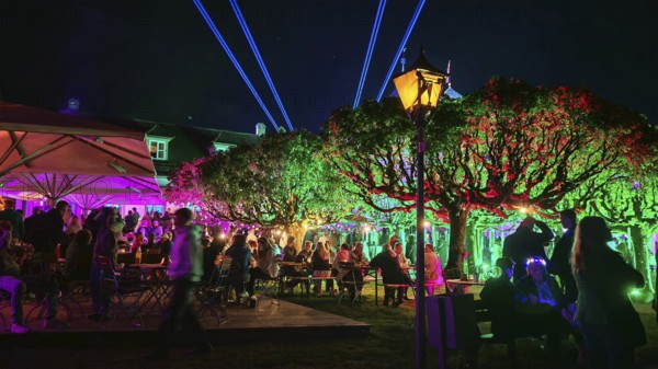 Colourfully lit garden at night, full of people, with atmospheric lighting, Kronach glows,