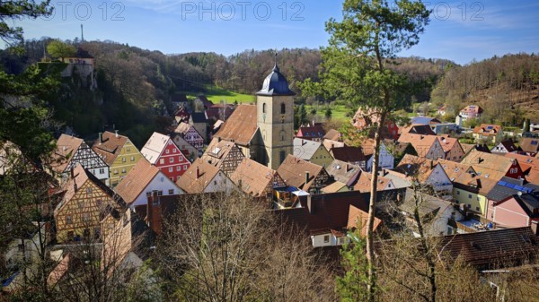 Picturesque village with colorful half-timbered houses and church tower, surrounded by hills, view