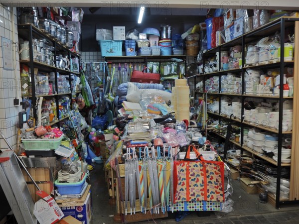 Small shop with a variety of everyday items on densely packed shelves and tables, Wet Market,