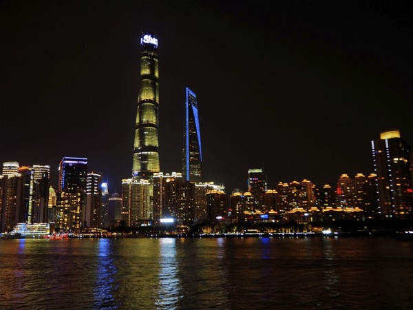 Illuminated city on riverbank at night with clear view of skyscrapers, Shanghai, China